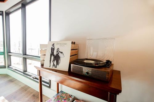 A record player with a vinyl album on a wooden table, near large windows with natural light.