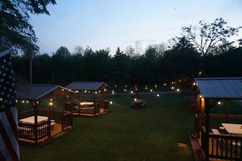 Twilight view of a serene outdoor space with wooden gazebos and string lights in a lush green setting.