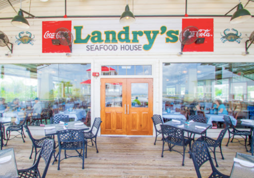 Exterior view of Landry's Seafood House with outdoor seating and large windows, featuring a Coca-Cola sign.