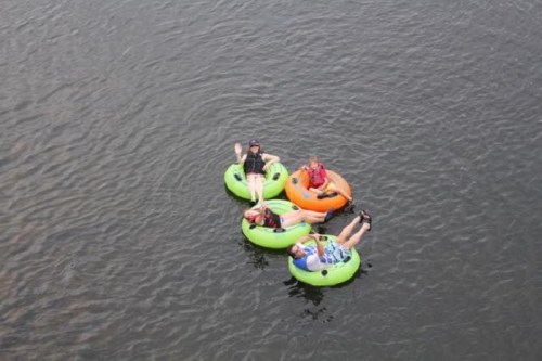 Four people relax on colorful inner tubes in a calm body of water, enjoying a sunny day.
