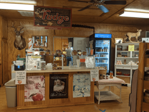 A cozy shop counter with fudge signage, snacks, and a display of various products in a wooden interior.