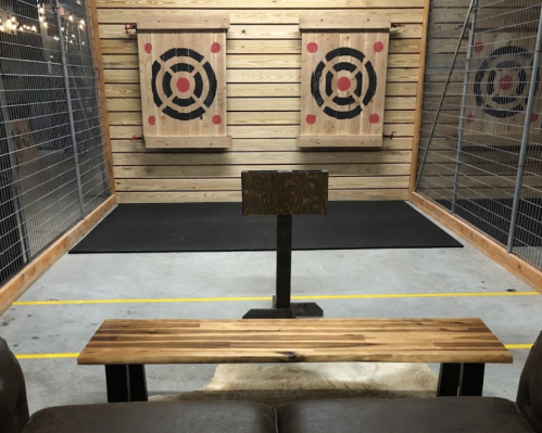 A wooden bench in front of two target boards in an indoor axe-throwing venue with a rustic wooden wall.