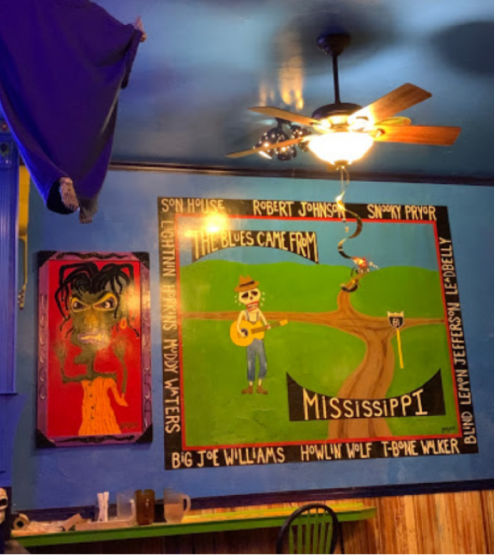 Colorful mural featuring blues legends and a scenic Mississippi theme, with a ceiling fan and blue walls in a cozy setting.