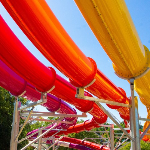 Colorful water slide tubes in shades of red, orange, and yellow against a clear blue sky.