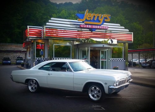 A classic white car parked in front of Jerry's Curb Service, a retro-style diner with vibrant signage.