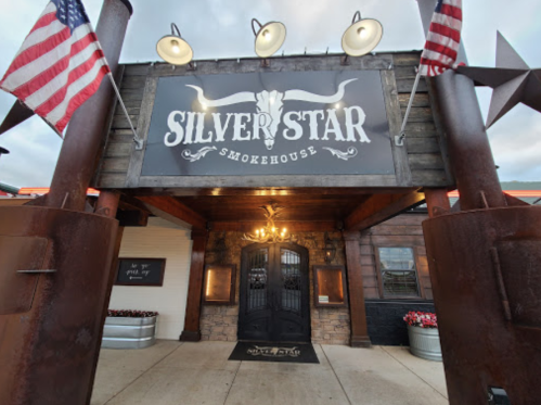 Exterior of Silver Star Smokehouse with a sign, flags, and decorative elements, set against a cloudy sky.