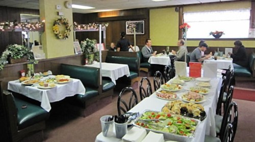 A cozy restaurant interior with green booths, tables set with food, and diners enjoying meals in a festive atmosphere.