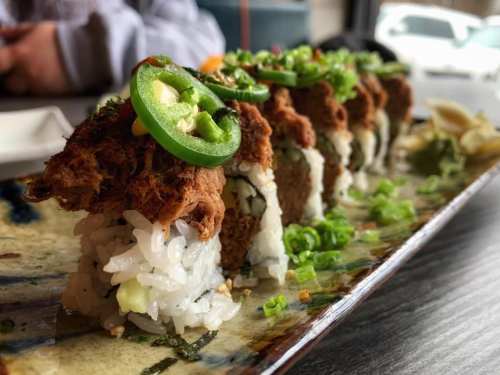 A platter of sushi rolls topped with sliced jalapeños and green onions, served on a decorative plate.
