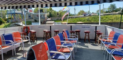 Outdoor seating area on a boat, featuring colorful chairs and bar stools with a scenic view in the background.