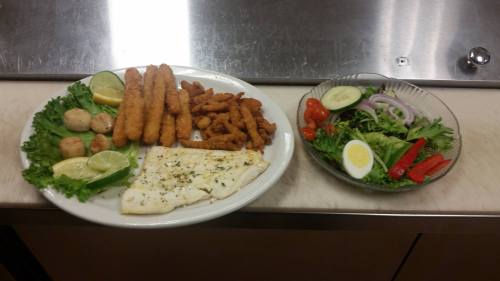 A plate with fried fish, shrimp, and lemon, alongside a fresh salad with tomatoes, cucumbers, and boiled egg.