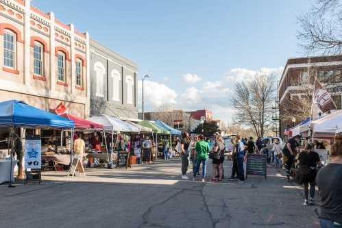 A bustling outdoor market with colorful tents, vendors, and visitors enjoying the sunny day.