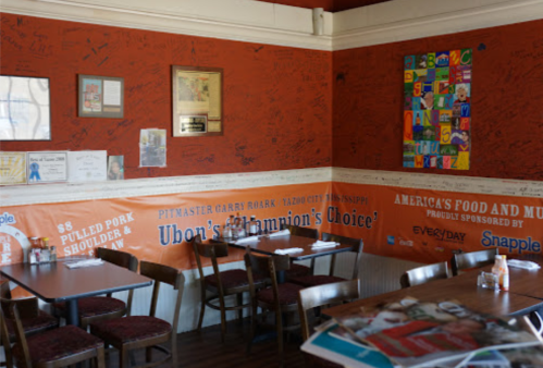 A cozy restaurant corner with signed walls, colorful artwork, and tables set for dining.