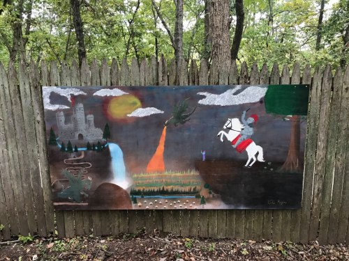 A colorful mural depicting a knight on a horse, dragons, a castle, and a vibrant landscape with trees and a waterfall.