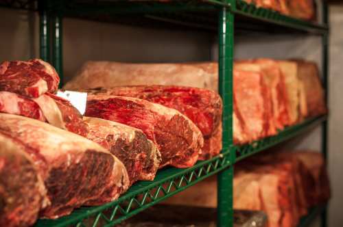 A display of various cuts of meat on green metal shelves in a refrigerated storage area.