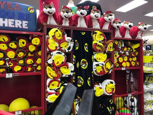 A display of plush toys and colorful blankets on shelves, featuring red and yellow designs in a store setting.
