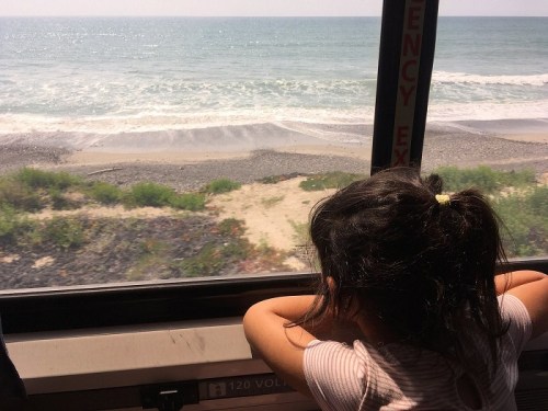 A child gazes out a bus window at a scenic view of the ocean and shoreline.