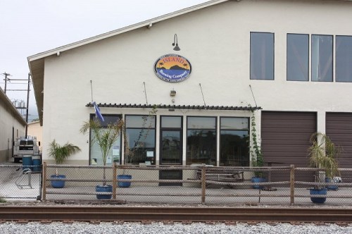 Exterior of a building with a sign reading "Island Sailing Center," featuring potted plants and a fence.