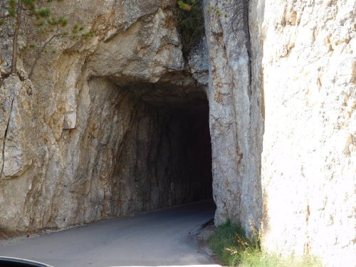 A narrow road passes through a rocky tunnel, surrounded by steep stone walls and greenery.