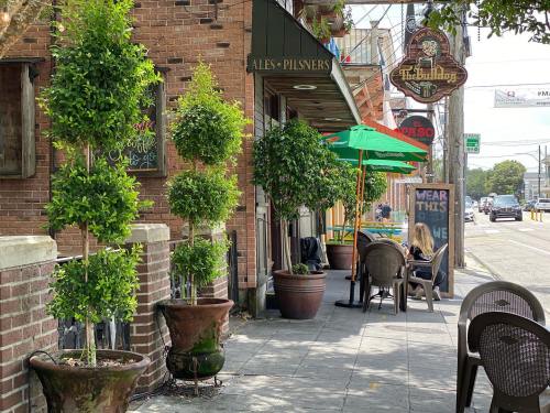 Outdoor seating area of a restaurant with potted plants, green umbrellas, and a brick facade on a sunny day.