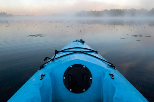 A blue kayak on a misty lake, surrounded by calm water and distant trees, creating a serene atmosphere.