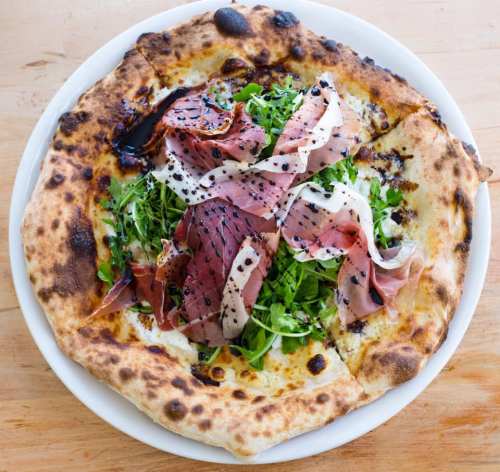 A pizza topped with fresh arugula, prosciutto, and drizzled with balsamic glaze on a rustic crust.