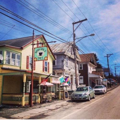Colorful café on a quiet street, with flags and parked cars under a clear blue sky.