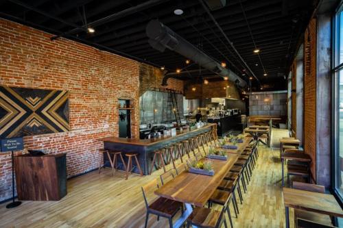 Modern restaurant interior with exposed brick walls, wooden tables, and a sleek bar area. Bright and inviting atmosphere.