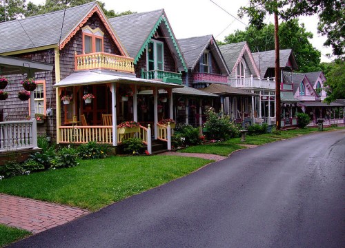 Colorful Victorian-style houses line a tree-shaded street, adorned with flowers and greenery.