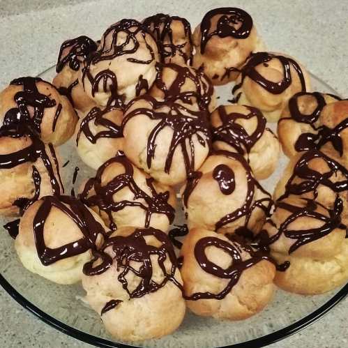 A plate of cream puffs drizzled with chocolate sauce, arranged in a circular pattern.