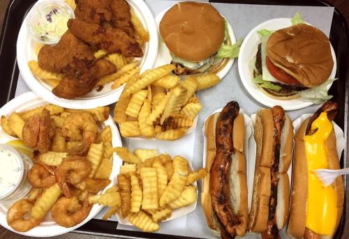 A tray of food featuring fried chicken, burgers, shrimp, crinkle-cut fries, and hot dogs with mustard.