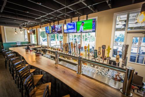 A modern bar with a wooden counter, multiple beer taps, and several TVs displaying sports. Bright and inviting atmosphere.