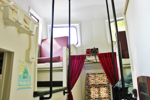 Interior of a small, bright space with two seating areas, curtains, and windows, featuring a cozy, vintage design.