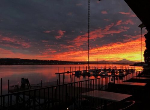 A vibrant sunset over a calm lake, with silhouetted boats and mountains in the background.