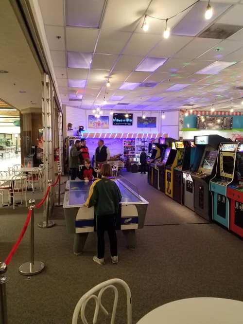 A colorful arcade with vintage games, featuring a child playing air hockey and others enjoying the space.
