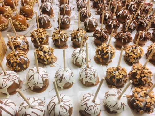 A variety of decorated caramel apples with nuts and drizzled chocolate, arranged neatly on a table.