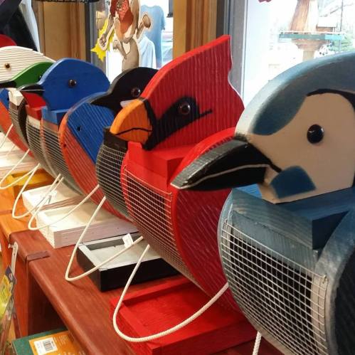Colorful wooden birdhouses shaped like various birds, lined up on a shelf with a bright, cheerful display.