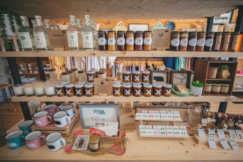 A cozy shop display featuring jars, candles, mugs, and various handmade items on wooden shelves.