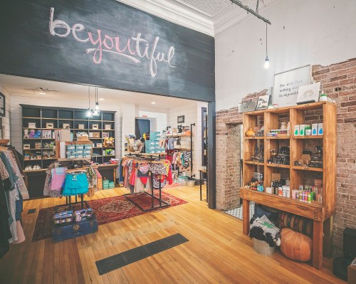 A cozy boutique interior featuring shelves of products, colorful clothing displays, and a chalkboard sign that says "beyoutiful."