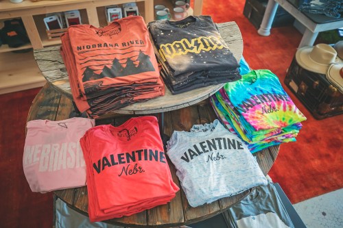 A display of folded t-shirts in various colors and designs, arranged on a wooden table in a retail setting.
