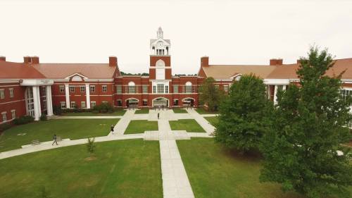 Aerial view of a red-brick academic building with a clock tower, surrounded by green lawns and pathways.
