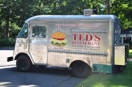A vintage food truck with a shiny silver exterior, featuring a logo for Ted's Restaurant and promoting steamed cheeseburgers.
