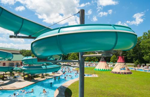 A water park scene featuring turquoise water slides, a lazy river, and colorful teepee structures under a blue sky.