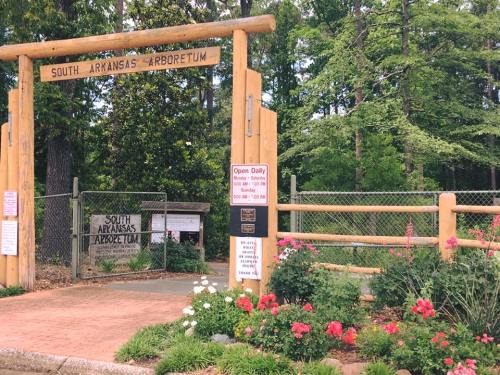 Entrance to South Arkansas Arboretum, featuring wooden archway and colorful flowers, surrounded by lush greenery.