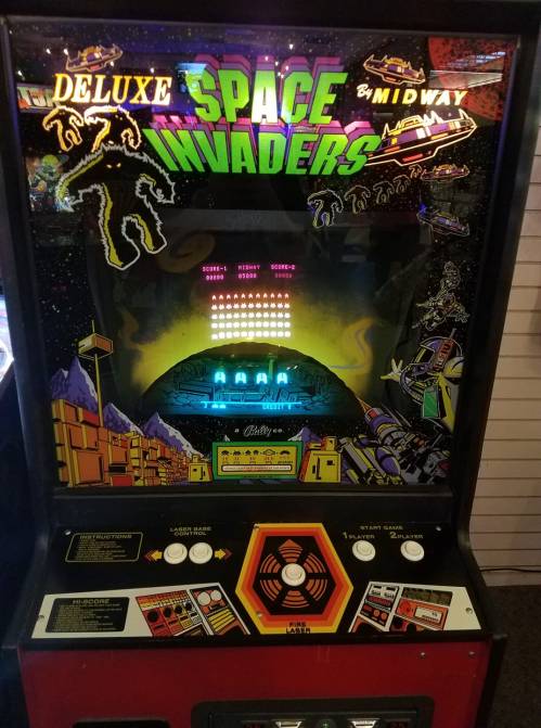A vintage arcade game cabinet for "Deluxe Space Invaders" featuring colorful graphics and control buttons.