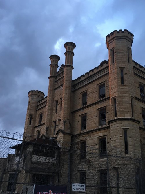 Historic stone building with towers, surrounded by a fence and cloudy sky, suggesting an abandoned or restricted site.