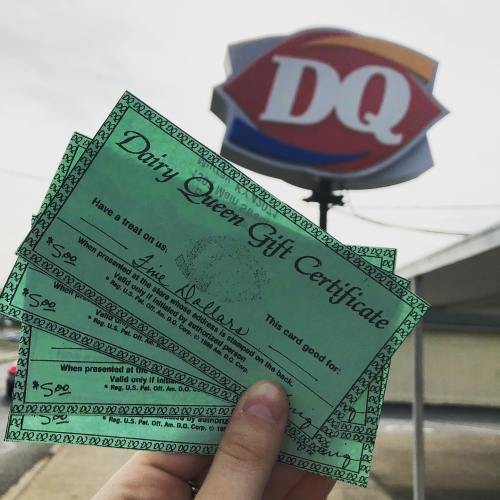 Three Dairy Queen gift certificates in front of a Dairy Queen sign.