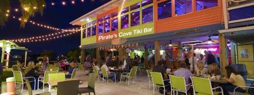 A vibrant tiki bar with colorful decor, outdoor seating, and string lights, bustling with patrons at night.