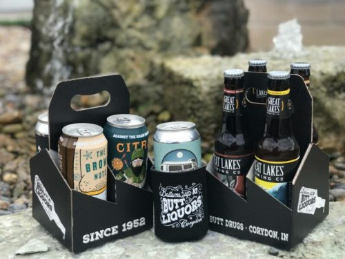 Two six-pack carriers of craft beer, featuring various cans, set against a rocky background. Text reads "Since 1952."