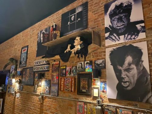 A wall decorated with vintage horror movie memorabilia, including posters, figurines, and a Dracula mannequin.