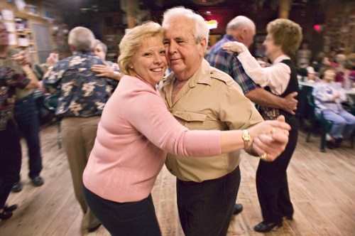 A joyful couple dances together in a lively social setting, surrounded by other dancers in a warm, inviting atmosphere.